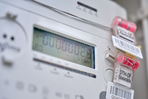 Ein digitaler Stromzähler zeigt den aktuellen Verbrauch in kWh an. Auf dem Zähler sind mehrere farbige Clips mit Barcodes angebracht. Der Bildschirm ist hell und gut lesbar, mit einer Anzeige von "000000.02 kWh".
