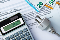 Ein Taschenrechner zeigt den Wert 183,29 an. Daneben liegt ein Stromstecker, und im Hintergrund sind Geldscheine (20 und 50 Euro) sowie ein Dokument mit Informationen zu Zahlungen zu sehen.