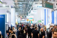 Eine belebte Messehalle mit vielen Personen, die zwischen Ständen von Firmen wie Vaillant und Bosch wandern. Die Atmosphäre ist geschäftig, und es sind zahlreiche Präsentationen und Informationsstände sichtbar, die Produkten und Dienstleistungen gewidmet sind.