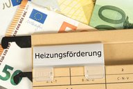 Ein Ordner mit dem beschrifteten Tab „Heizungsförderung“ liegt auf einem Untergrund aus verschiedenen Euro-Banknoten. Die Banknoten sind teilweise sichtbar und verleihen der Szene einen finanziellen Kontext.