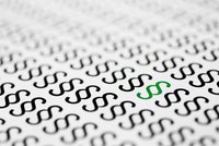 Auf dem Bild sind mehrfach das Paragraphenzeichen „§“ abgebildet, das in schwarz gedruckt ist. Eines der Paragraphenzeichen ist jedoch in grün hervorgehoben. Der Hintergrund ist hell und besteht aus vielen wiederholten Mustern des Paragraphenzeichens.