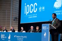 Ein Redner steht an einem Pult während der 40. Sitzung des IPCC in Kopenhagen. Im Hintergrund sitzen mehrere Personen an einem Tisch. Die Bühne ist mit dem IPCC-Logo und Informationen zur Veranstaltung dekoriert.