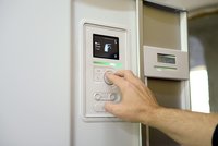 Eine Hand dreht einen Regler an einem modernen Kühl- und Gefriergerät. Auf einem digitalen Bildschirm sind Symbole und Informationen angezeigt, darunter Optionen wie "normal" und "Luxus". Das Gerät wirkt technisch fortschrittlich und benutzerfreundlich.