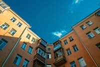 Ein Blick in einen Innenhof eines Mehrfamilienhauses. Die orangefarbenen Wände sind mit vielen Fenstern ausgestattet, und der Himmel darüber ist klar und blau, mit einigen weißen Wolken.