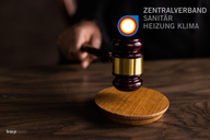 Ein Gerichtshammer wird auf einer Holzplatte geschlagen. Im Hintergrund ist das Logo des Zentralverbandes Sanitär, Heizung, Klima sichtbar. Die Hand, die den Hammer hält, ist teilweise im Bild zu sehen.