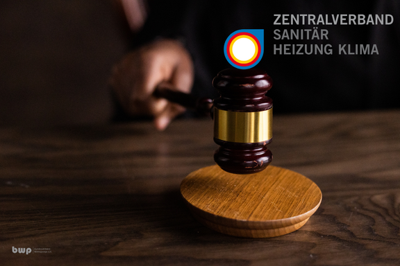 Ein Gerichtshammer wird auf einer Holzplatte geschlagen. Im Hintergrund ist das Logo des Zentralverbandes Sanitär, Heizung, Klima sichtbar. Die Hand, die den Hammer hält, ist teilweise im Bild zu sehen.