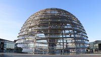 Das Bild zeigt die Reichstagskuppel in Berlin. Die gläserne, spiralförmige Struktur ermöglicht Besuchern einen Rundblick auf die Stadt. Die Kuppel ist auf mehreren Ebenen zugänglich und spiegelt die Umgebung wider. Der Himmel ist blau mit wenigen Wolken.