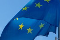 Die europäische Flagge weht im Wind. Sie besteht aus einem blauen Hintergrund mit einem Kranz von zwölf goldenen Sternen, die in einem Kreis angeordnet sind. Der Himmel ist klar und blau, was die Farben der Flagge hervorhebt.