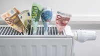 Auf einem Heizkörper stecken zusammengerollte Geldscheine in verschiedenen Werten (5, 10, 20, 50 und 100 Euro). Der Heizkörper hat einen Thermostat auf der rechten Seite. Das Bild vermittelt eine humorvolle Sichtweise auf Heizkosten.